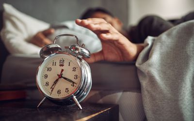 Photo of a man in bed reaching for his alarm clock to illustrate the article 